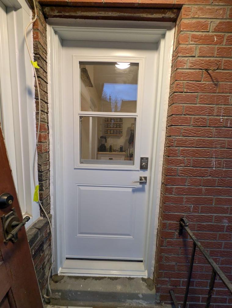 After: new white insulated front door with a window, keypad deadbolt and lever handle, set in fresh white trim in a brick wall