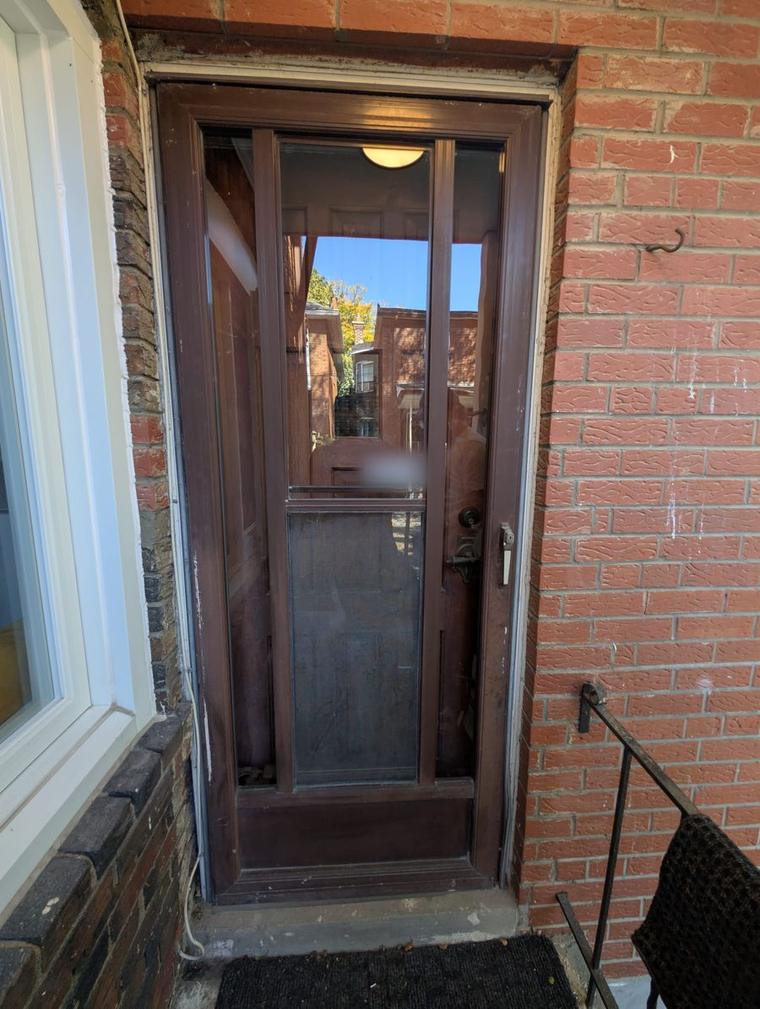 Before: worn brown aluminum storm door over an old wood front door in a brick wall