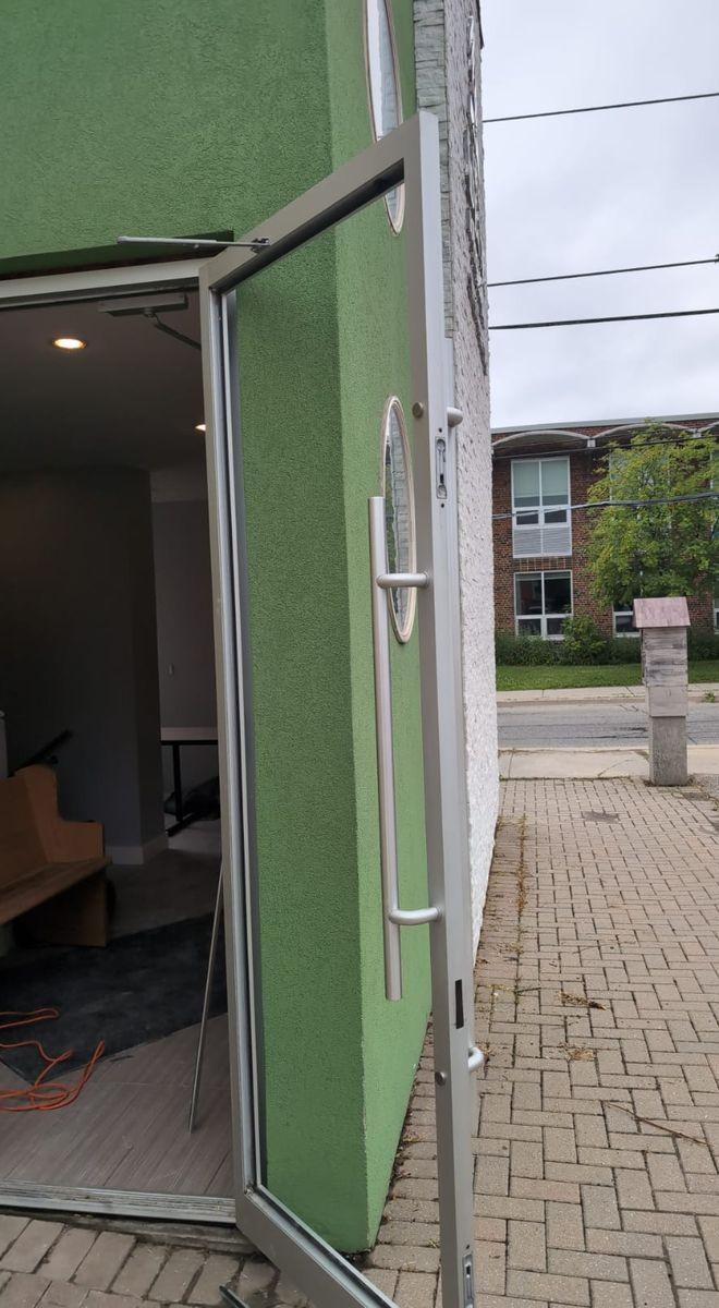 Before: aluminum storefront entrance door standing open with no glass in its frame, on a green building