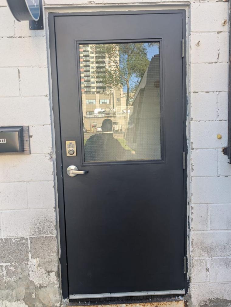 After: new black steel door with a large wired-glass window, keypad deadbolt and lever handle on a white block wall